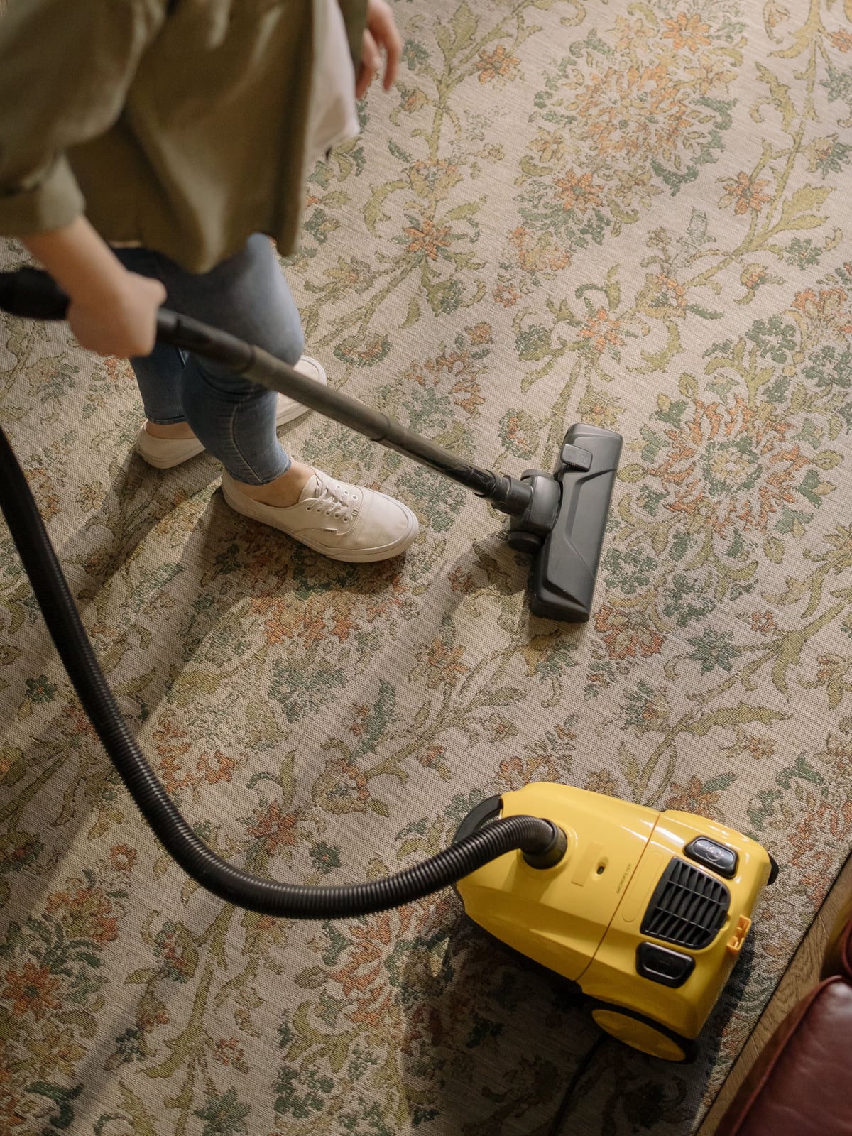 An operator cleaning a patterned carpet with a yellow canister vacuum