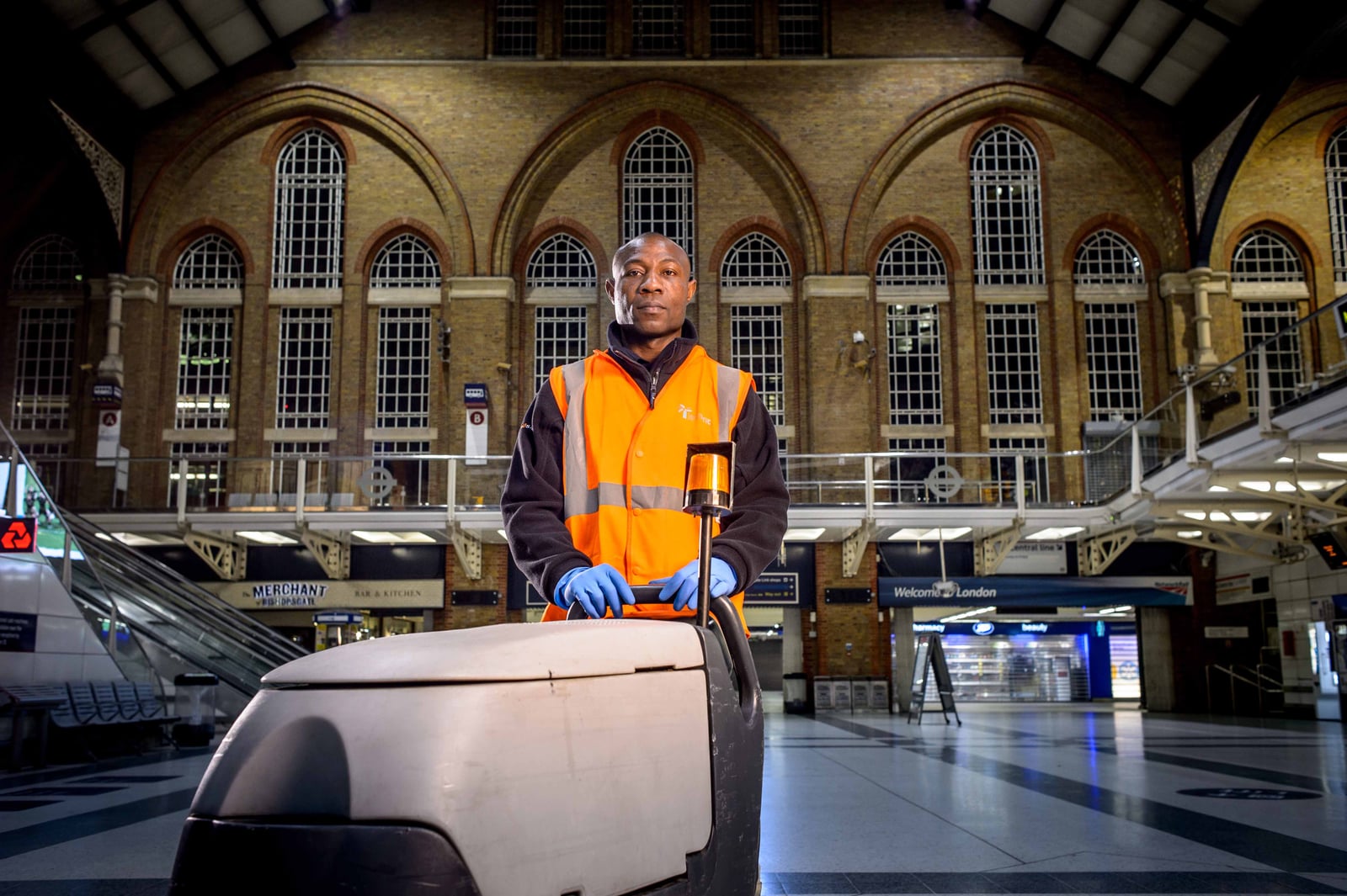 A professional operator using a ride-on floor-cleaning machine across a large public concourse