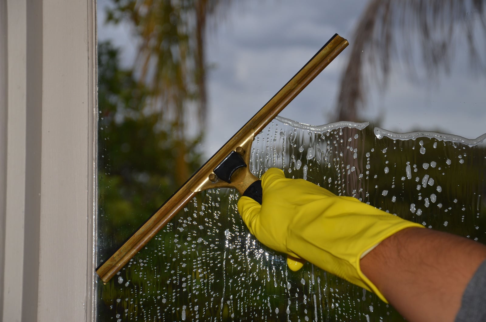 A gloved hand removing cleaning solution from a window with a squeegee